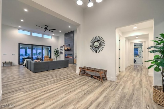 living room with light hardwood / wood-style flooring, a large fireplace, ceiling fan, and a high ceiling