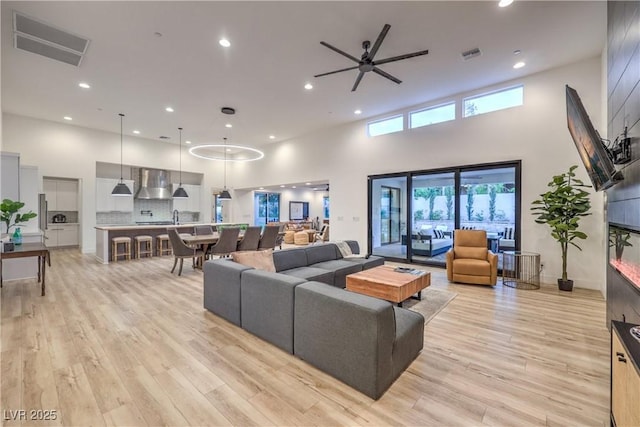 living room with a towering ceiling, light hardwood / wood-style floors, and ceiling fan