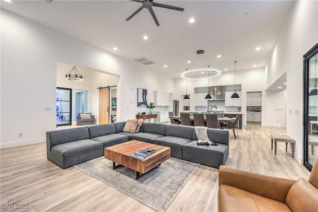 living room with light hardwood / wood-style floors, a barn door, ceiling fan, and a high ceiling