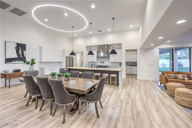 dining area with a towering ceiling, sink, and light hardwood / wood-style flooring