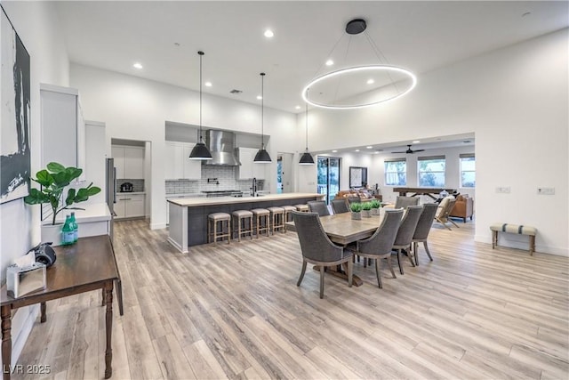 dining space with a high ceiling, sink, ceiling fan, and light hardwood / wood-style flooring