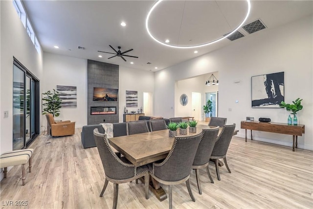 dining space featuring light hardwood / wood-style flooring, a towering ceiling, a fireplace, and ceiling fan