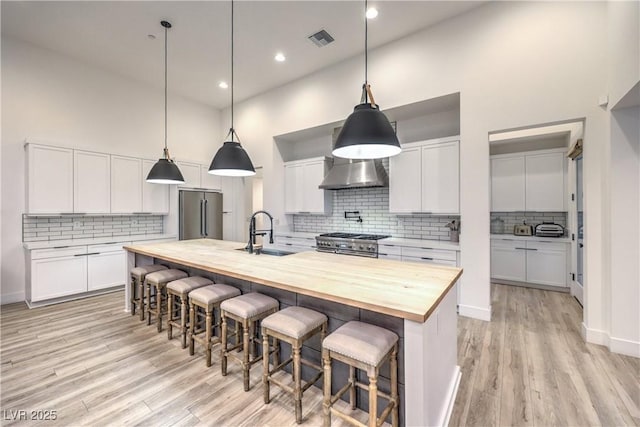 kitchen with white cabinetry, sink, wooden counters, high end appliances, and a kitchen island with sink