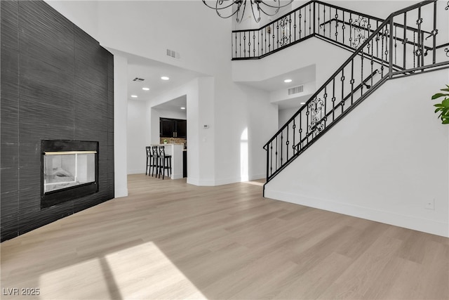 unfurnished living room with a chandelier, wood-type flooring, a towering ceiling, and a fireplace