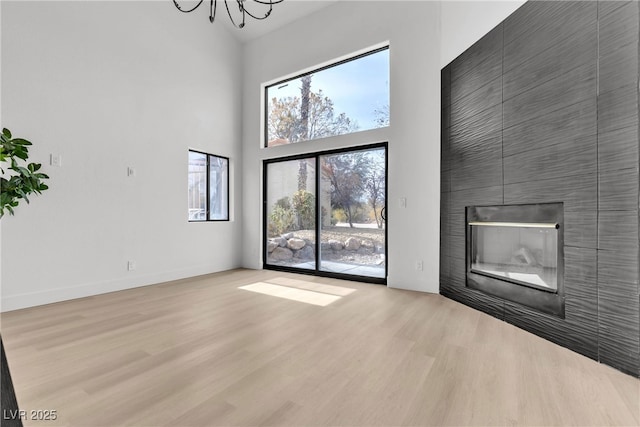 unfurnished living room with a fireplace, a towering ceiling, a chandelier, and light hardwood / wood-style flooring