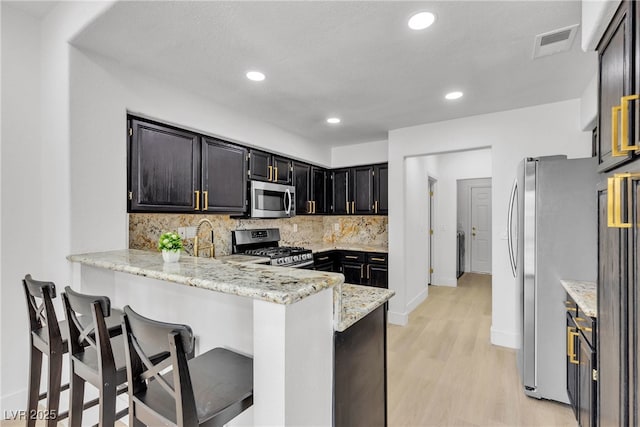 kitchen with stainless steel appliances, kitchen peninsula, light stone countertops, a breakfast bar area, and tasteful backsplash