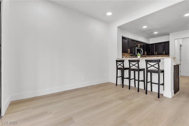 kitchen with kitchen peninsula, backsplash, a kitchen breakfast bar, and light hardwood / wood-style flooring