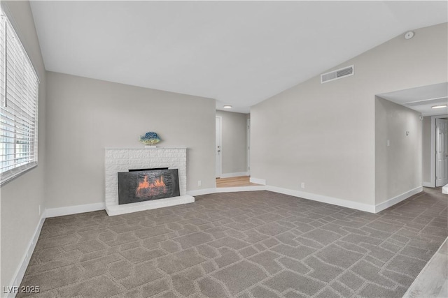 unfurnished living room featuring lofted ceiling, a brick fireplace, and carpet floors