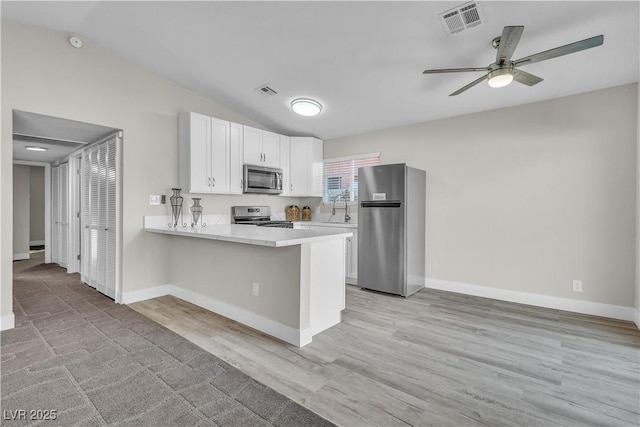 kitchen with lofted ceiling, appliances with stainless steel finishes, white cabinets, and kitchen peninsula