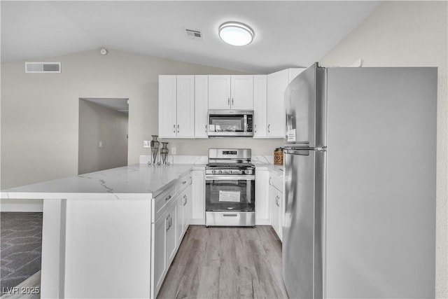 kitchen with light stone counters, vaulted ceiling, appliances with stainless steel finishes, kitchen peninsula, and white cabinets