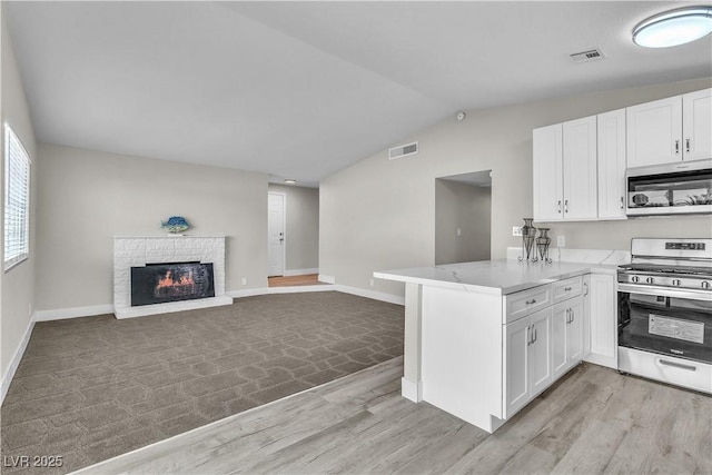 kitchen with lofted ceiling, appliances with stainless steel finishes, white cabinetry, a fireplace, and kitchen peninsula