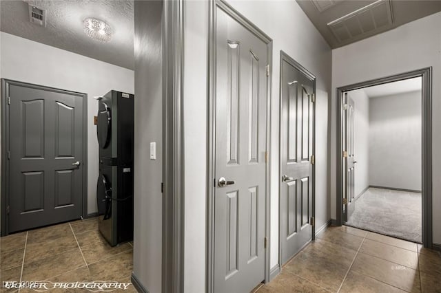 corridor with stacked washer / dryer, dark tile patterned flooring, and a textured ceiling