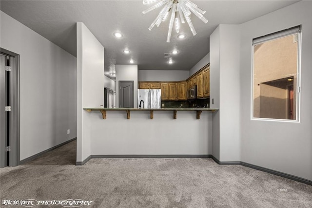 kitchen featuring dark carpet, stainless steel appliances, kitchen peninsula, and a kitchen bar