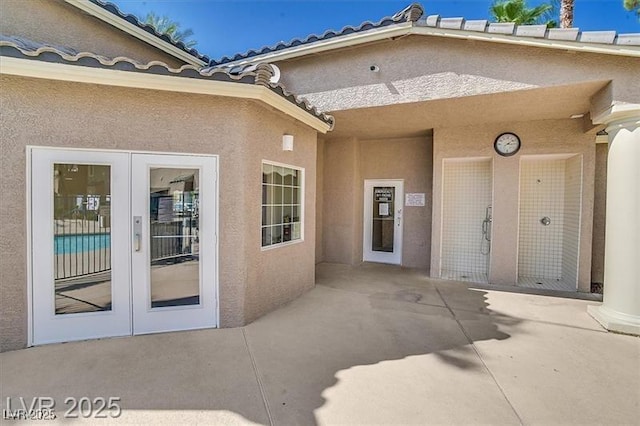 view of exterior entry with french doors, a patio area, a tiled roof, and stucco siding