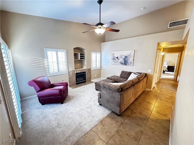 living room featuring ceiling fan, light tile patterned flooring, a fireplace with flush hearth, visible vents, and baseboards