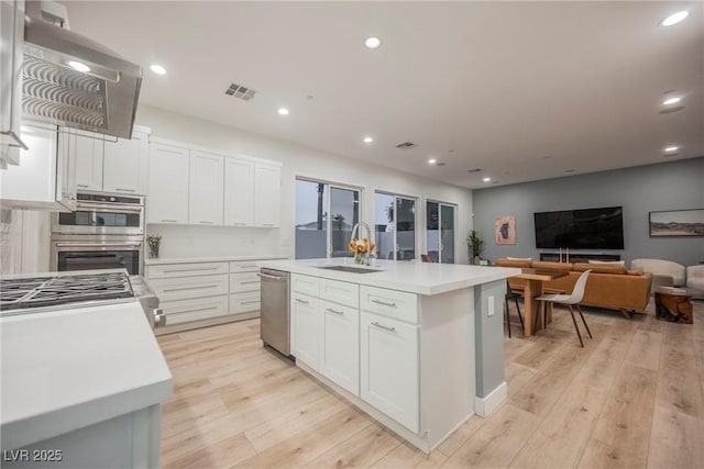 kitchen with white cabinetry, sink, a center island with sink, and light hardwood / wood-style floors