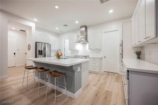 kitchen featuring appliances with stainless steel finishes, white cabinetry, a kitchen breakfast bar, a center island with sink, and wall chimney exhaust hood