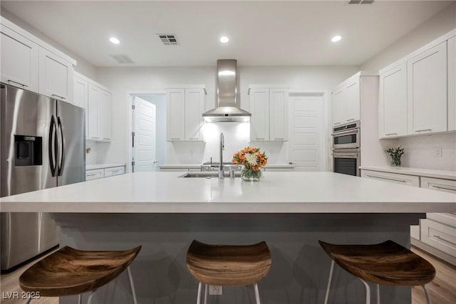 kitchen featuring stainless steel appliances, an island with sink, a breakfast bar area, and wall chimney range hood