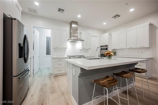 kitchen featuring sink, white cabinetry, stainless steel refrigerator with ice dispenser, a center island with sink, and wall chimney exhaust hood