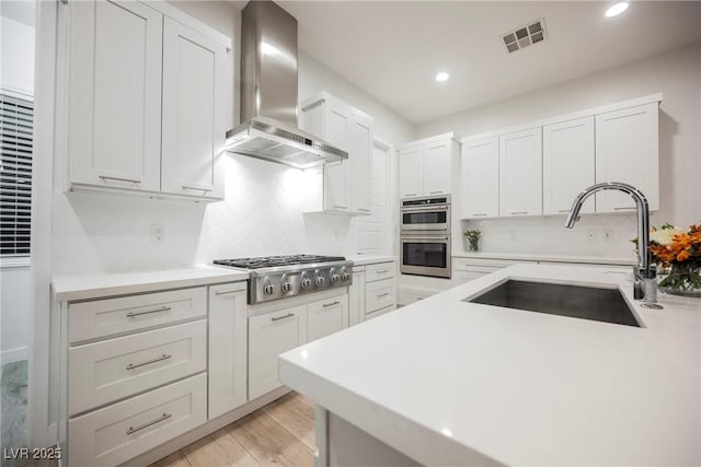 kitchen with wall chimney exhaust hood, stainless steel appliances, sink, and white cabinets