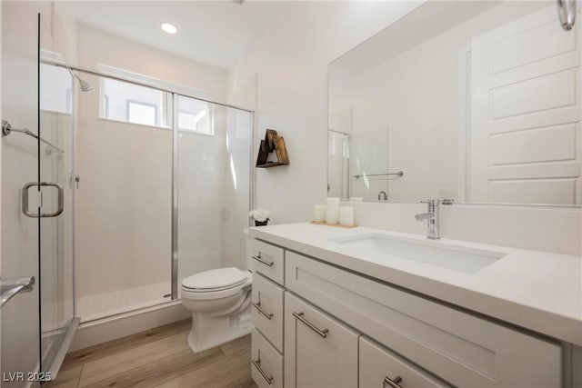 bathroom with wood-type flooring, a shower with shower door, vanity, and toilet