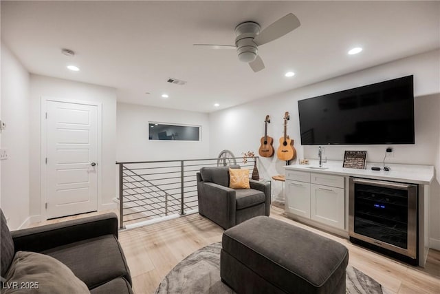 living room with sink, beverage cooler, ceiling fan, and light hardwood / wood-style flooring