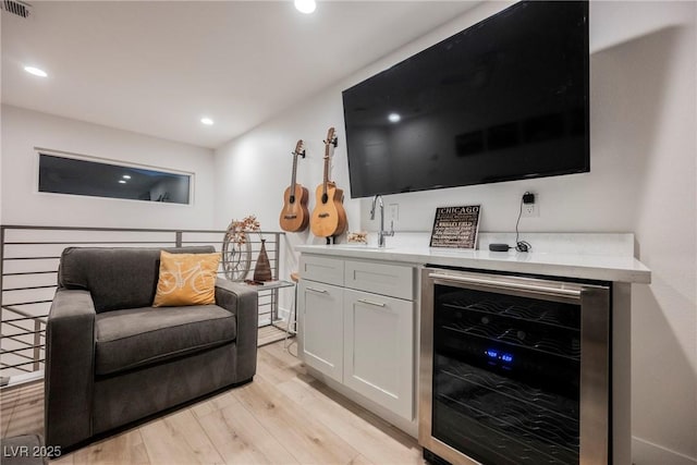 bar featuring white cabinetry, beverage cooler, and light hardwood / wood-style floors