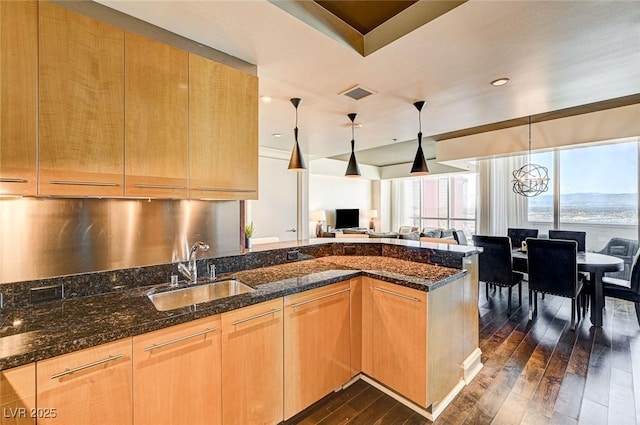 kitchen with sink, dark stone countertops, a chandelier, dark hardwood / wood-style flooring, and hanging light fixtures