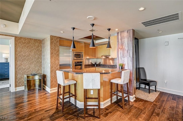 kitchen featuring appliances with stainless steel finishes, a kitchen breakfast bar, dark hardwood / wood-style flooring, and hanging light fixtures