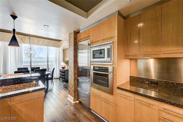 kitchen with built in appliances, decorative light fixtures, dark hardwood / wood-style flooring, a notable chandelier, and dark stone counters