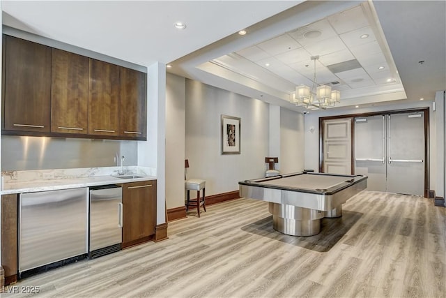 game room with pool table, a raised ceiling, light hardwood / wood-style flooring, and indoor wet bar