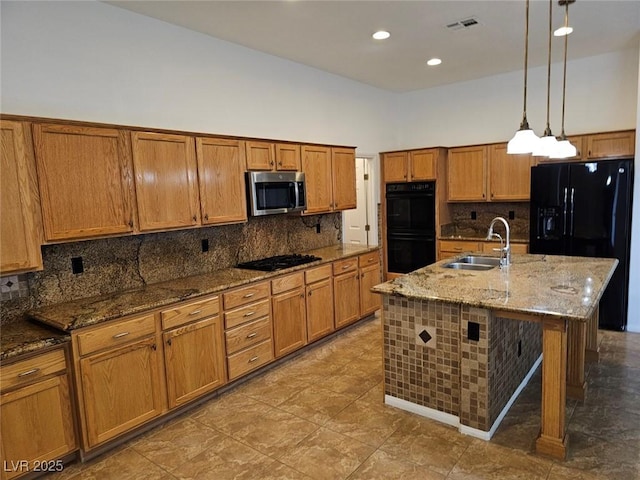 kitchen featuring sink, stone countertops, decorative light fixtures, a center island with sink, and black appliances