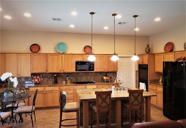 kitchen featuring sink, hanging light fixtures, tasteful backsplash, black appliances, and an island with sink