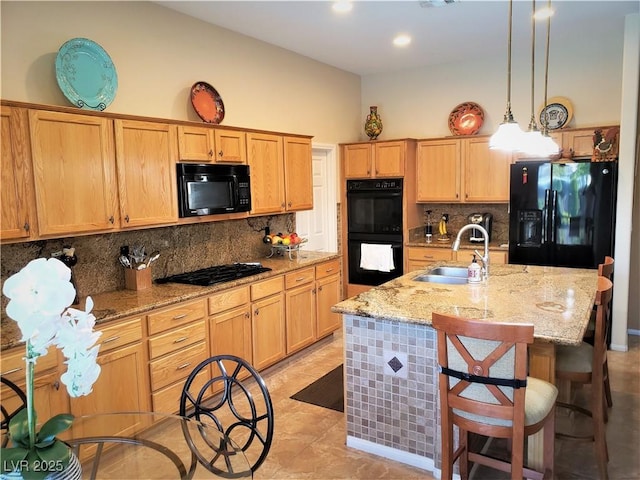 kitchen featuring sink, tasteful backsplash, a center island with sink, pendant lighting, and black appliances