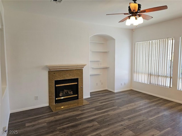 unfurnished living room featuring a tile fireplace, ceiling fan, built in features, and dark hardwood / wood-style flooring