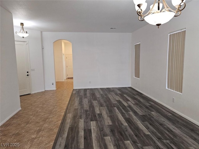 empty room with a notable chandelier and dark wood-type flooring