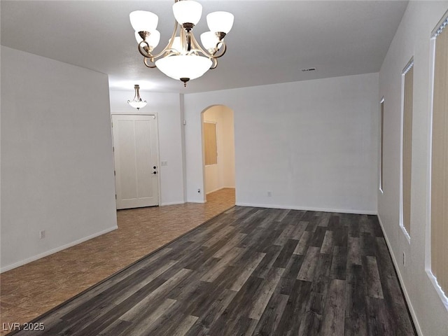 spare room with dark wood-type flooring and an inviting chandelier