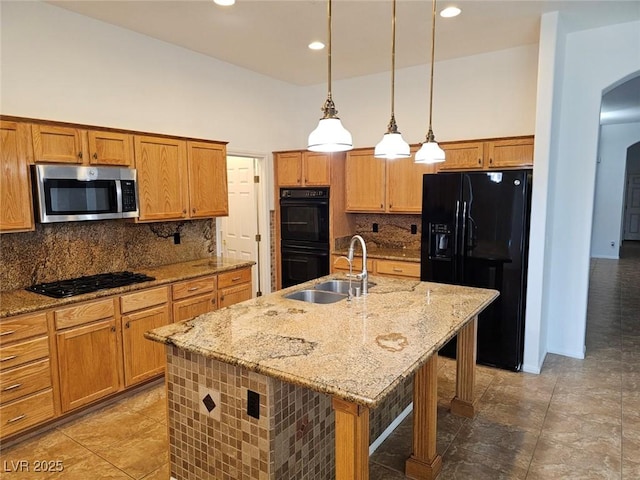 kitchen featuring sink, a center island with sink, black appliances, a kitchen bar, and decorative light fixtures