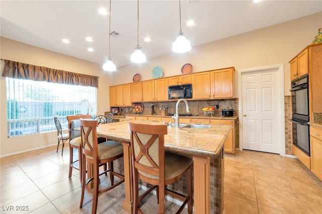 kitchen with pendant lighting, tasteful backsplash, sink, black appliances, and a center island with sink