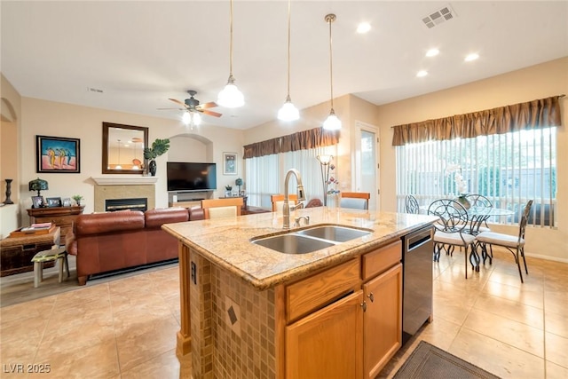 kitchen with pendant lighting, dishwasher, sink, a kitchen island with sink, and light stone countertops