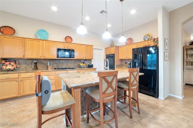 kitchen featuring light stone counters, hanging light fixtures, black appliances, and a center island with sink