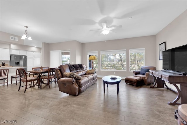 living room featuring ceiling fan with notable chandelier and light hardwood / wood-style flooring