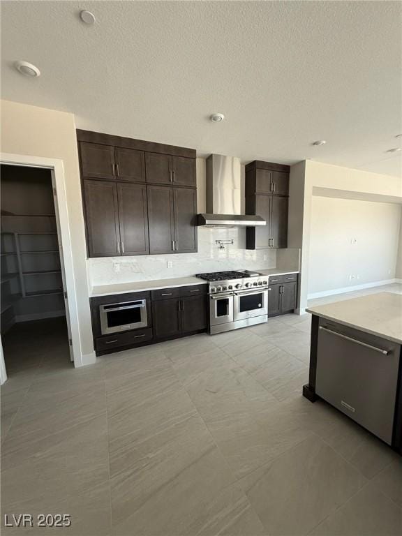 4630 Blushing Dawn Ave, Las Vegas, NV 89118 - kitchen featuring wall chimney range hood, stainless steel appliances, backsplash, dark brown cabinetry, and a textured ceiling