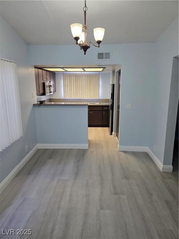 kitchen with pendant lighting, dark brown cabinetry, kitchen peninsula, and light hardwood / wood-style flooring