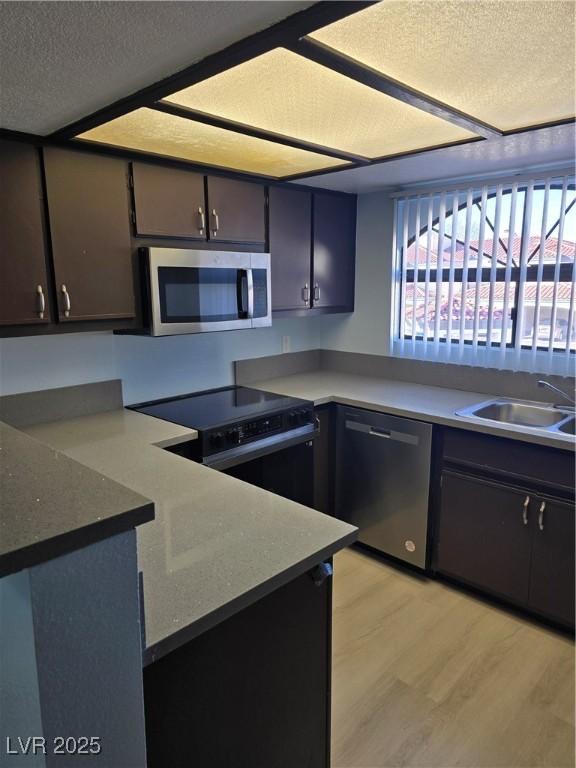 kitchen with appliances with stainless steel finishes, sink, dark brown cabinets, a textured ceiling, and light hardwood / wood-style flooring