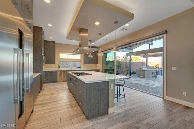 kitchen featuring decorative light fixtures, island exhaust hood, stainless steel appliances, light stone countertops, and a spacious island