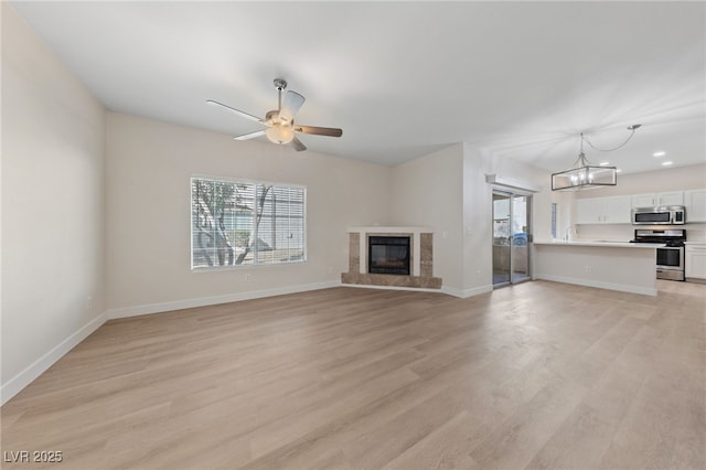 unfurnished living room with a fireplace, ceiling fan with notable chandelier, and light hardwood / wood-style flooring