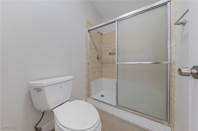 bathroom featuring a shower with door and toilet