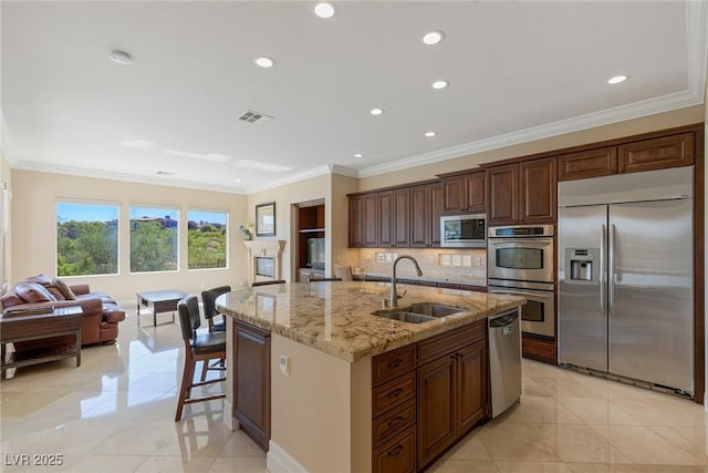 kitchen featuring sink, light stone counters, built in appliances, an island with sink, and backsplash