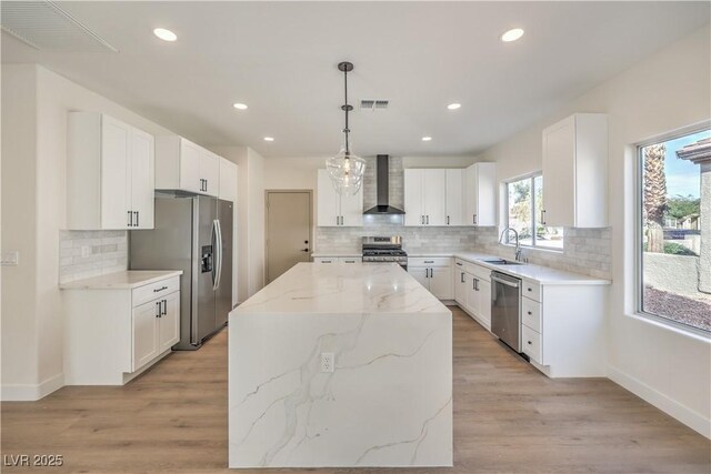 kitchen with appliances with stainless steel finishes, white cabinets, hanging light fixtures, a center island, and wall chimney exhaust hood